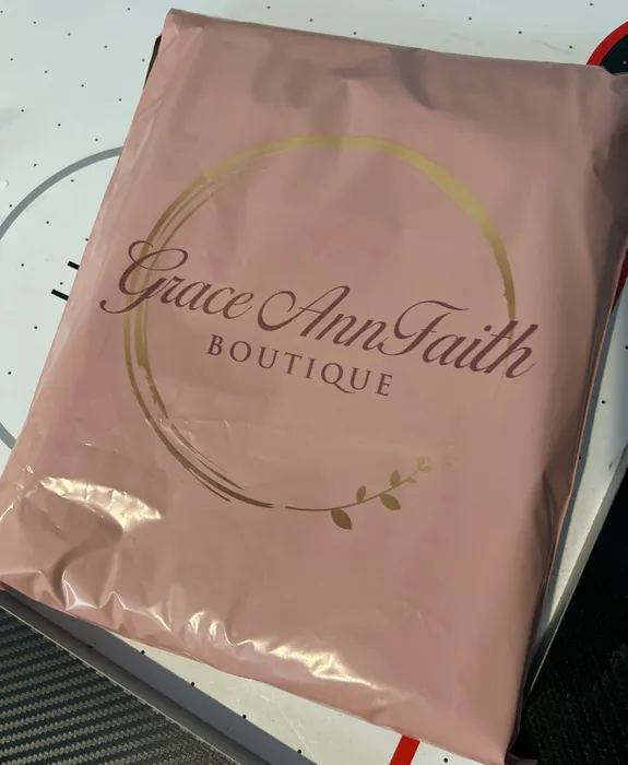 A pink custom poly mailer with 'Grace Ann Faith BOUTIQUE' printed in a decorative font, featuring a circular gold accent and decorative elements. The context suggests a business packaging theme.